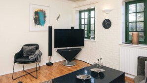 A living room with a flat-screen TV, a black coffee table, a black chair, and a green window. - Hotel Fanobad With Free Water Park Access (Fano)