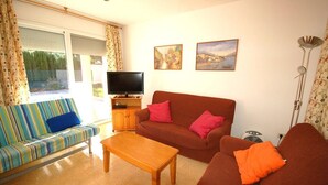 A living room with a striped sofa, a brown sofa with orange cushions, a wooden coffee table, a TV on a wooden cabinet, and two framed pictures on the wall. - SAONA VILLAS (VN DO) : villa 6 personnes, 500 m de la mer, climatisation, wifi (Tres Calas)