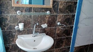 Une salle de bain avec un lavabo blanc, un miroir et un mur recouvert de carreaux de marbre.