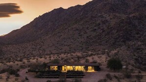 Une maison moderne dotée d’un toit plat, entourée d’un paysage aride et vallonné.