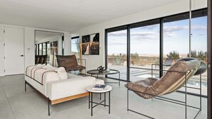 Un salon moderne comprenant un canapé, un fauteuil, une petite table et de grandes fenêtres donnant sur le désert.