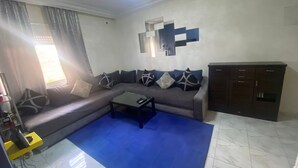Een woonkamer met een bank, een bijzettafeltje, een kast en een blauw vloerkleed.