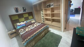 Een slaapkamer met een bed, nachtkastje, een groen vloerkleed en een houten garderobe met planken.