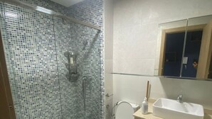 Een badkamer met een douchecabine van glas, een toilet, een wastafel en een spiegel boven de wastafel.