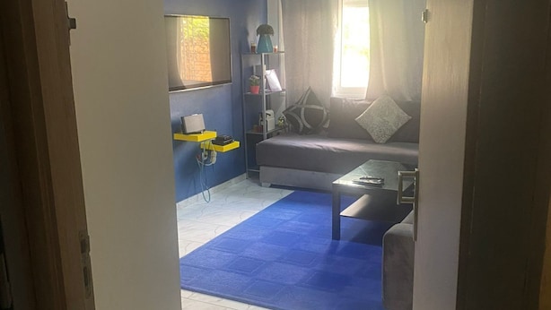 Een woonkamer met een blauw tapijt, een bank, een salontafel en een televisie aan de muur.
