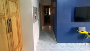 Een gang met een houten garderobe, een blauwe wand met een tv en een betegelde vloer.