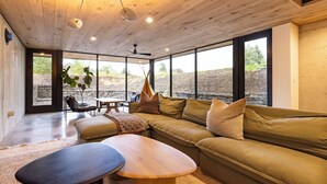 Un vaste espace de vie doté d’un plafond en bois, de grandes fenêtres, d’un canapé, d’une table basse et offrant une vue sur l’extérieur.