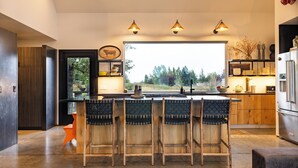 Une cuisine moderne dotée d’un îlot central, de tabourets de bar, de meubles en bois et de luminaires suspendus.