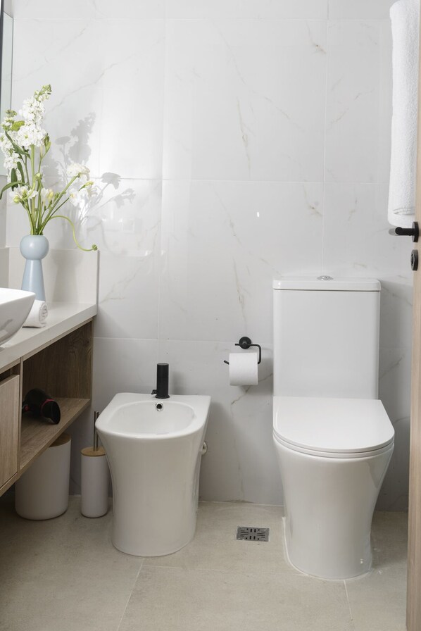 Ein Badezimmer mit Toilette, Bidet, Waschbecken und einer Vase mit Blumen auf der Ablagefläche.