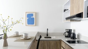Uma cozinha moderna com bancadas brancas, uma cafeteira preta e um quadro abstrato na parede.