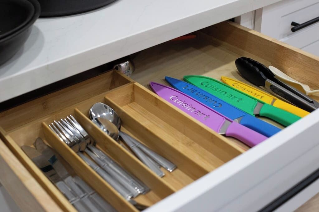 A drawer with utensils and kitchen tools, including forks, spoons, and a knife with a green handle.