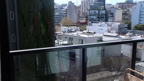 Un balcon doté d’une balustrade en verre, de deux fauteuils en osier et d’une petite table ronde.