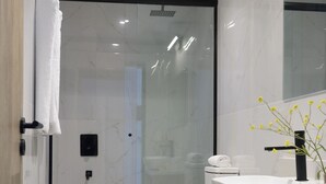 Une salle de bain moderne avec une douche à l’italienne en verre, un lavabo blanc avec un robinet noir et un meuble-lavabo en bois.