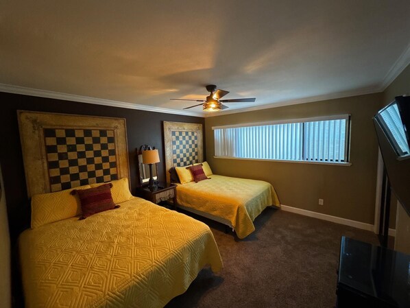 A hotel room with two beds, a ceiling fan, a large window with blinds, and a television on a stand. - Dock Holiday – The Keys Favorite | Wild West River Escape (Parker)
