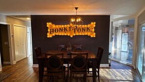 A dining area with a table and chairs, a chandelier, and a wall sign that reads "HONKITONK." - Dock Holiday – The Keys Favorite | Wild West River Escape (Parker)