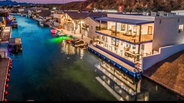 Ein Haus am Wasser mit Anlegesteg, Booten und mehreren Etagen sowie Balkonen.