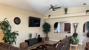 A living room with a sofa, TV, and plants. - Chippy, Saltwater Pool & Hot tub (Lake Havasu City)