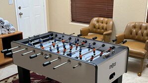 A foosball table in a room with a patterned rug, two leather chairs, and a door in the background. - Chippy, Saltwater Pool & Hot tub (Lake Havasu City)
