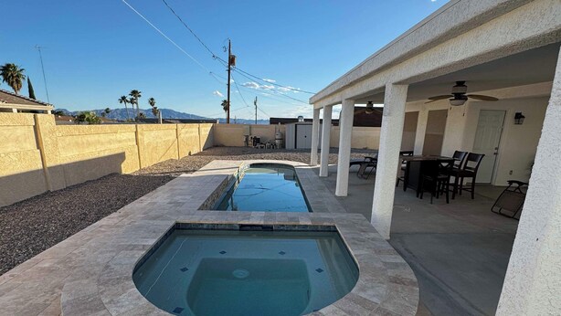 A swimming pool with a stone surround, a covered patio area with chairs and tables, and a view of mountains in the background. - Chippy, Saltwater Pool & Hot tub (Lake Havasu City)