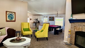 A living room with a pool table, yellow chairs, a fireplace, and a kitchen in the background. - Cliff Hanger, River access with dock (Parker)