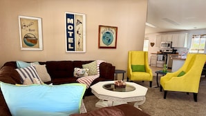 A living room with a brown couch, a yellow armchair, a coffee table, and a kitchen in the background. - Cliff Hanger, River access with dock (Parker)