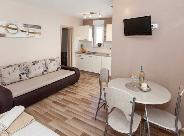 A modern living room with a sofa, a dining table with chairs, a TV mounted on the wall, and a kitchen in the background. - Beachfront Apartments for Relaxing Getaways in Crikvenica (Crikvenica)