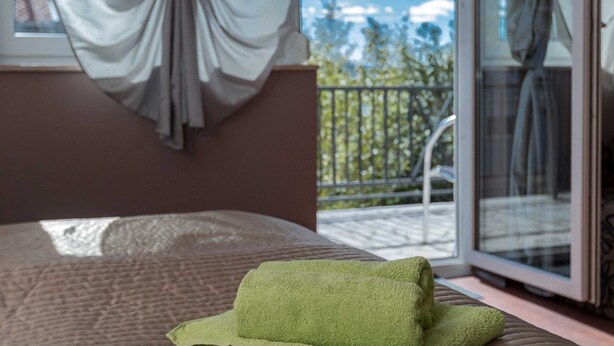A bedroom with a bed, a window with curtains, and a view of a balcony and trees. - Beachfront Crikvenica Apartments With Sea View (Crikvenica)