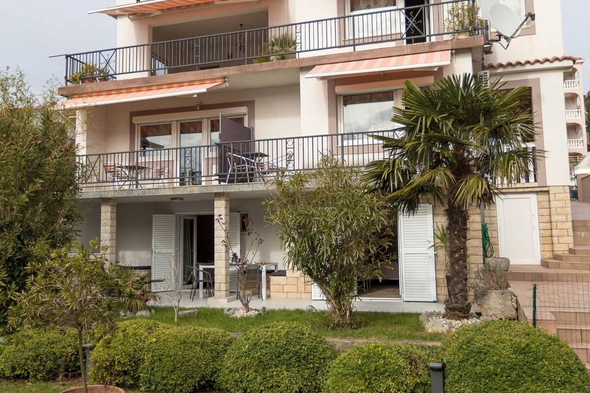 Un immeuble résidentiel à plusieurs étages, doté de balcons, d’un espace extérieur aménagé pour s’asseoir et d’un jardin bien entretenu.