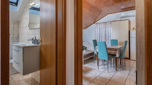 Une cuisine moderne dotée d’un évier et de meubles encastrés, un coin repas avec une table et des chaises, et un plafond en pente avec des poutres en bois.