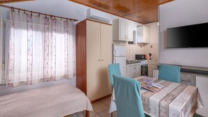 Une pièce de taille modeste comprenant un lit, une table avec des chaises, un coin cuisine et un téléviseur fixé au mur.