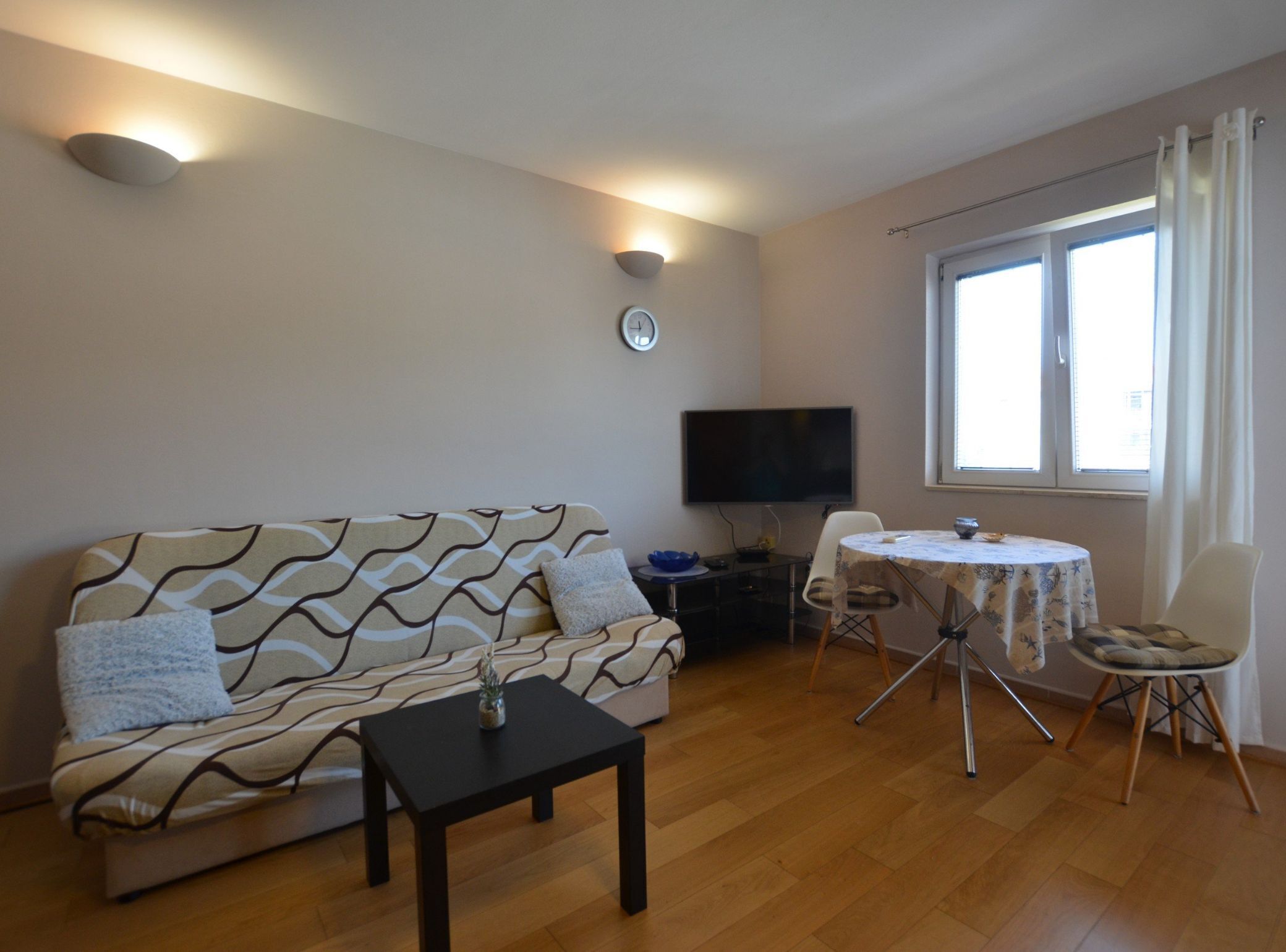 Ein Wohnzimmer mit einer Couch, einem kleinen Tisch, einem Fernseher und einem Fenster mit Vorhängen.