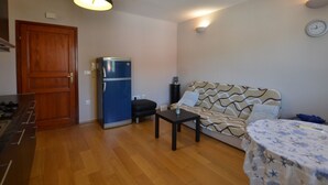 A compact living space with a wooden floor, a sofa, a small table, a refrigerator, a wooden door, and a wall clock. - Charming Retreat Near Rovinj With Private Balcony (Rovinj)