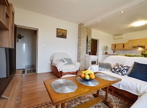 A modern living room with a sofa, a dining table with a fruit bowl, a kitchen area, and a hallway. - Family-friendly Apartment Near Rovinj (Rovinj)
