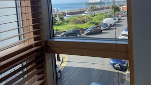 Vista desde una ventana con persianas de madera, que da a un estacionamiento con varios coches y un edificio lejano con una cúpula.