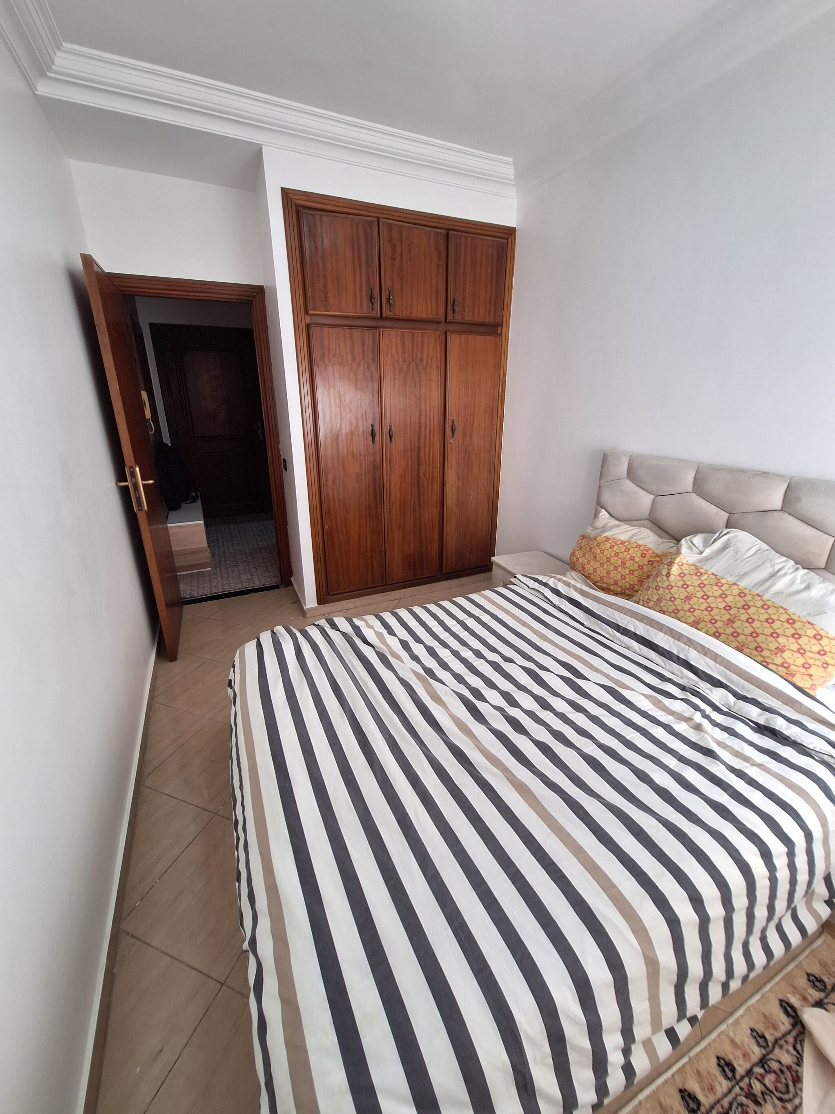 Un dormitorio con una cama grande, un armario de madera y una puerta que da a otra habitación.