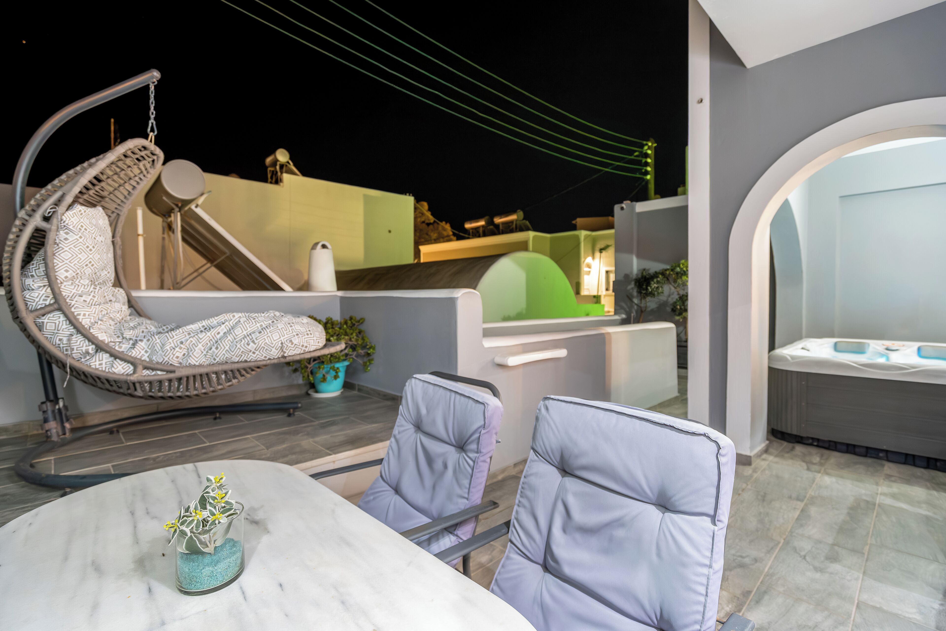 A modern outdoor seating area with a table, chairs, a hanging chair, and a hot tub.
