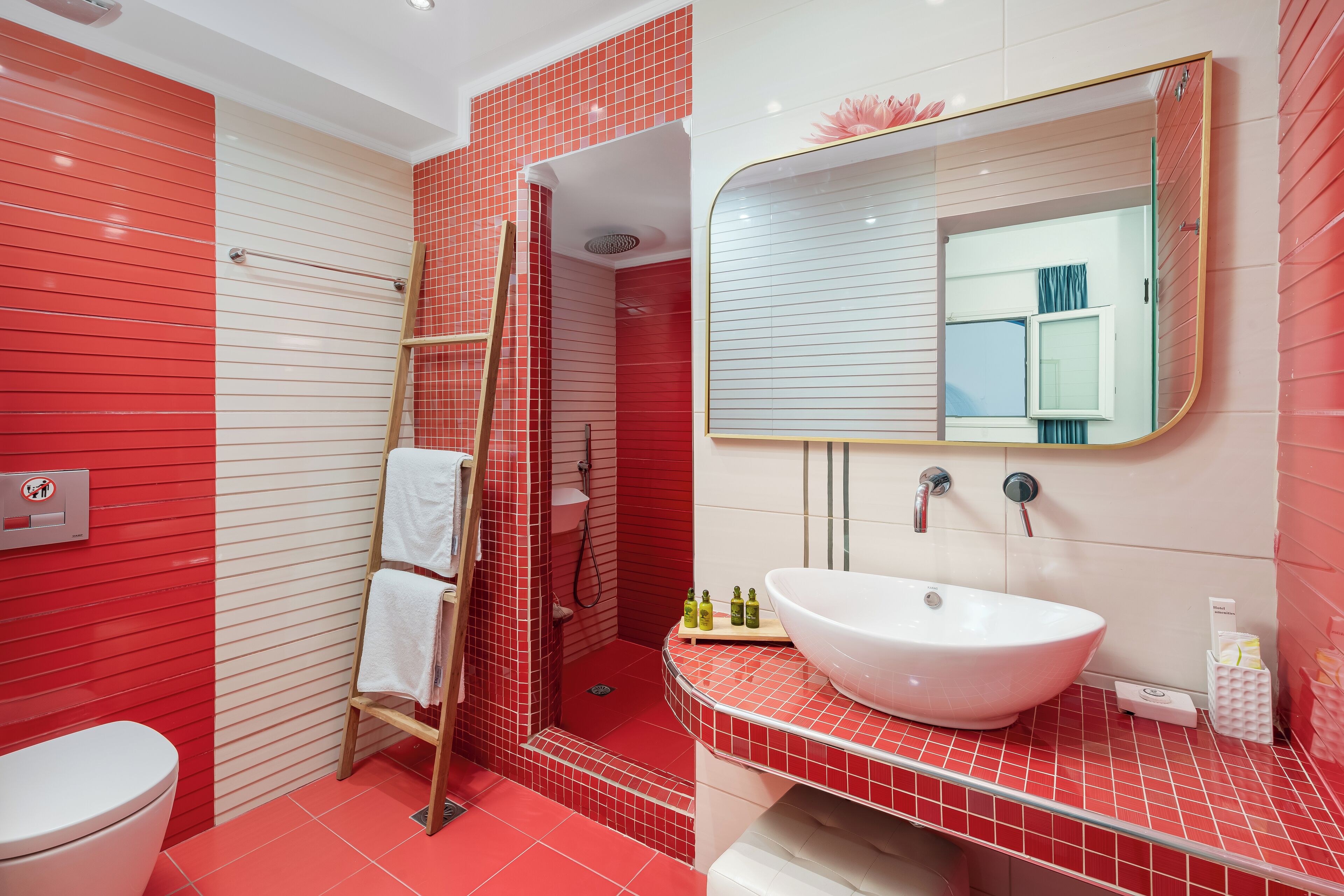 A bathroom with a red and white tiled design, a white sink, a mirror, and a shower area.