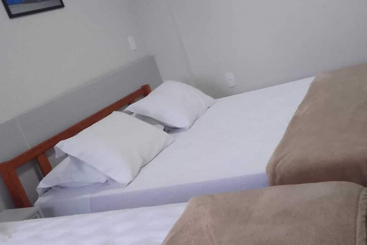 A single bed with a wooden frame, white bedding, and a beige blanket.