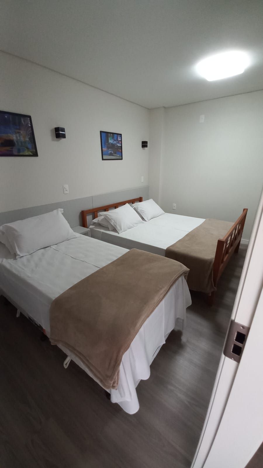 Ein Hotelzimmer mit zwei Einzelbetten, einem Holzkopfteil, einem kleinen Tisch und einer Wandleuchte.