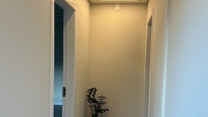 Un pasillo estrecho con suelo de madera, paredes blancas y una planta en maceta.