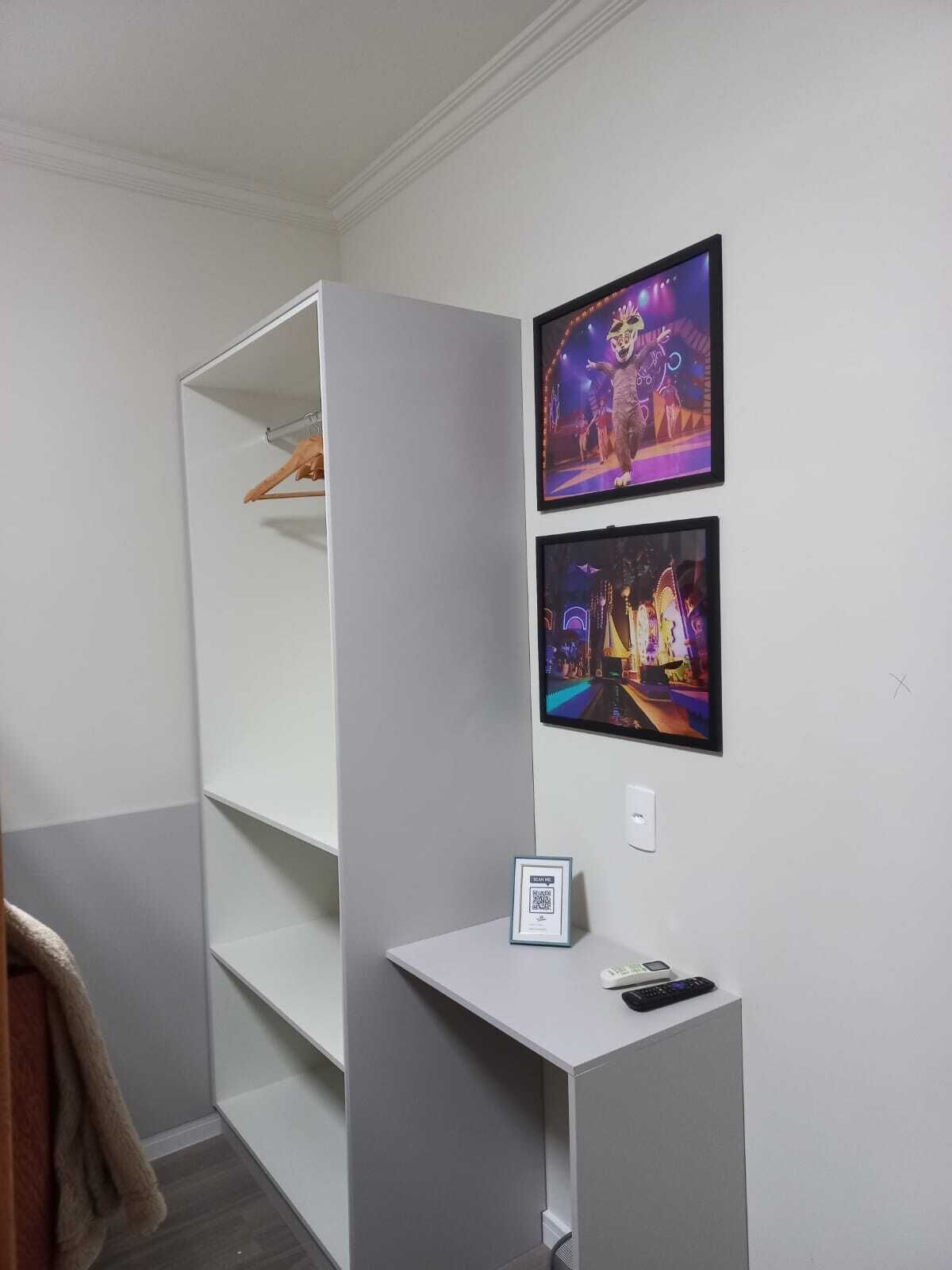 A room with a white wardrobe, a desk with a phone and a small framed picture, and two framed pictures on the wall.