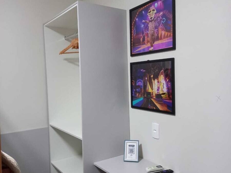 A room with a white wardrobe, a desk with a phone and a small framed picture, and two framed pictures on the wall.