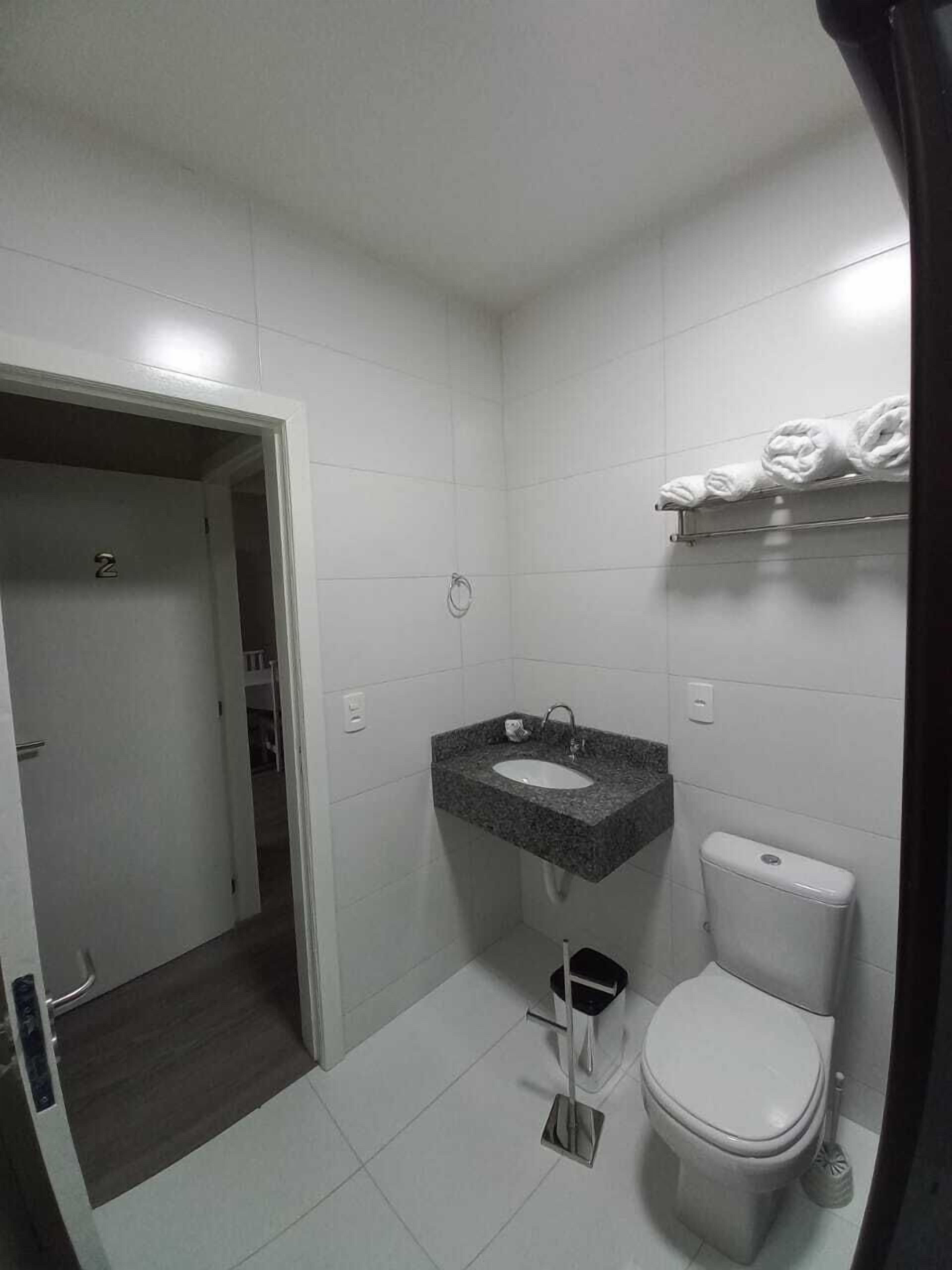 A small, modern bathroom with white tiles, a granite sink, a toilet, and a towel rack.