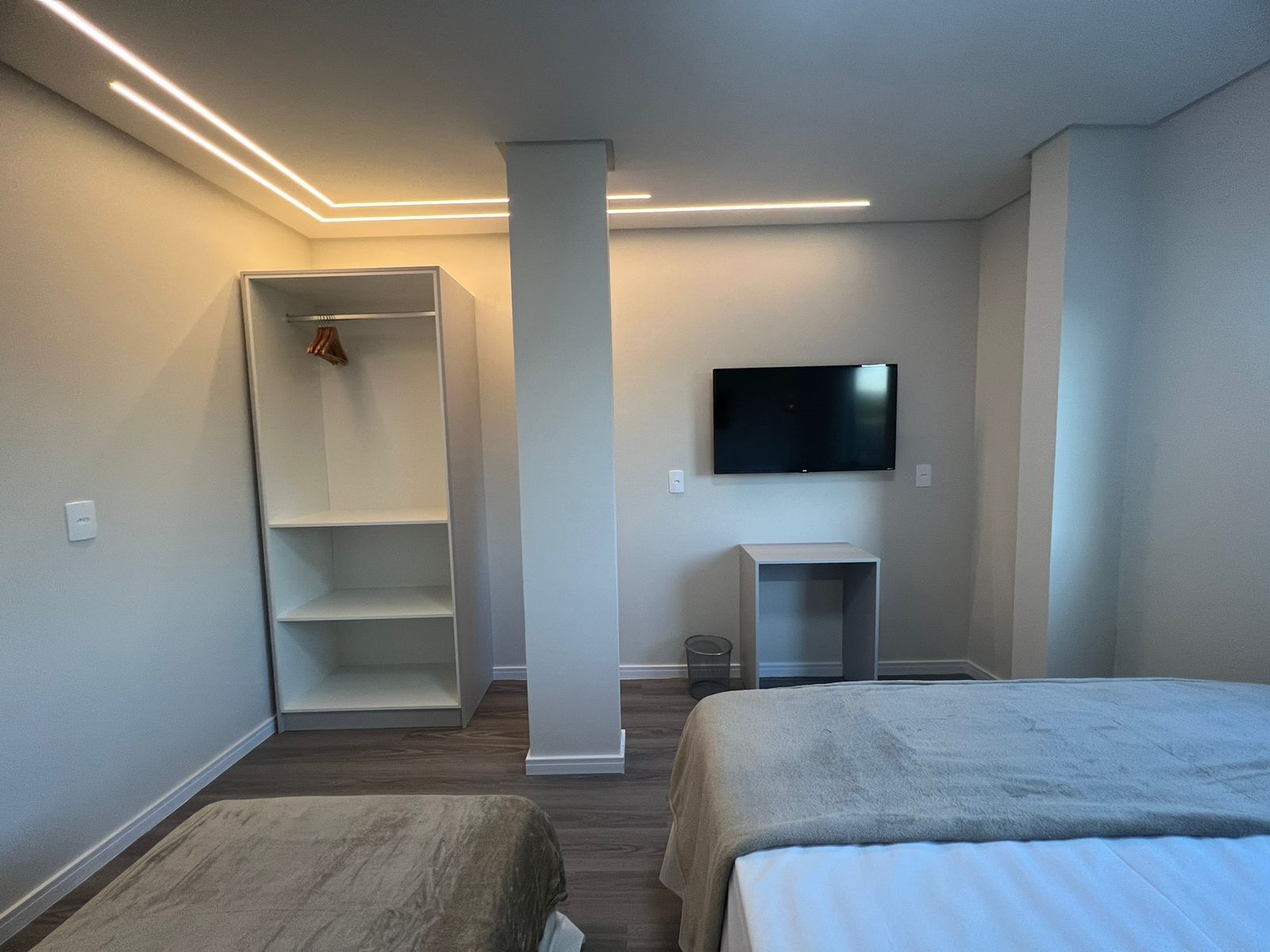 A modern bedroom with a bed, a TV mounted on the wall, and a wardrobe.