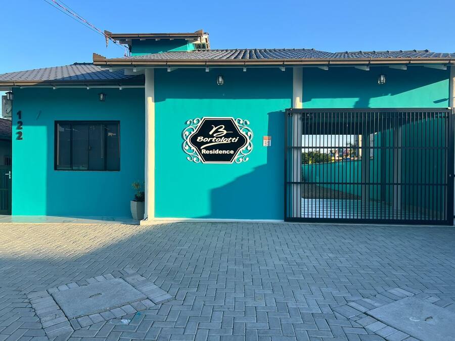 A residential building with a teal facade, a gated entrance, and a sign indicating 'Bortolotti Residence'.