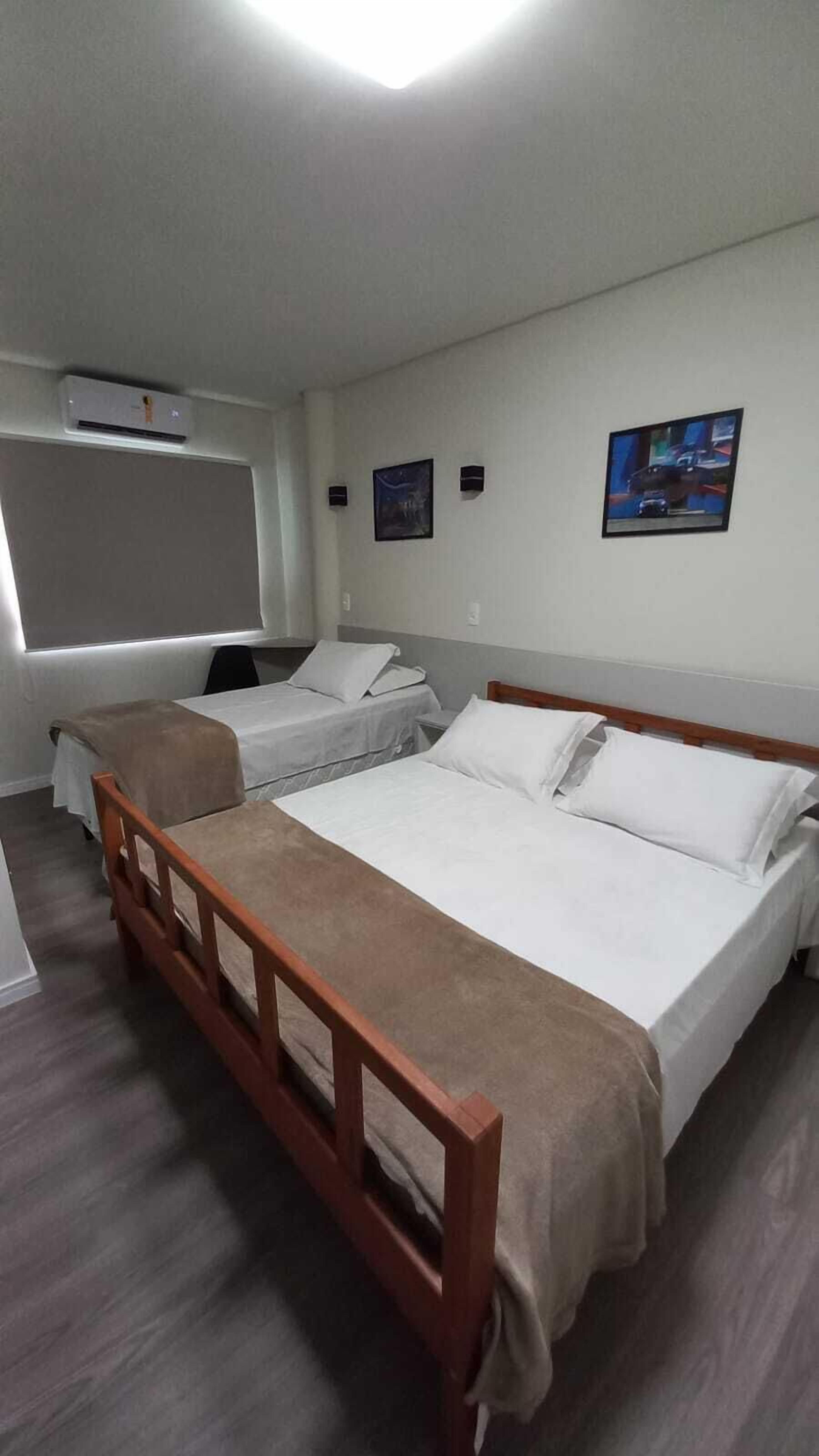 Habitación de hotel con dos camas individuales, cabecera de madera, ventana grande, unidad de aire acondicionado y televisor de pantalla plana montado en la pared.