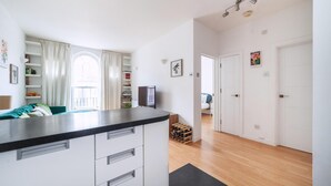 Eine moderne Küche mit weißen Schränken, einer schwarzen Arbeitsplatte und Blick auf einen Wohnbereich mit Sofa und Vorhängen.