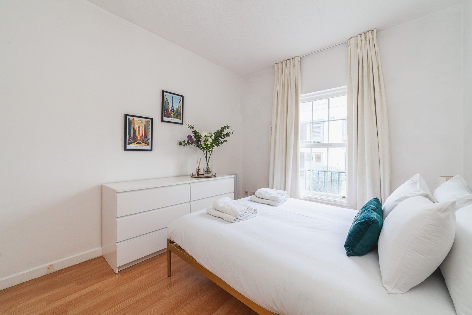 Une chambre à coucher au style minimaliste, avec un lit, une commode et une fenêtre avec des rideaux.