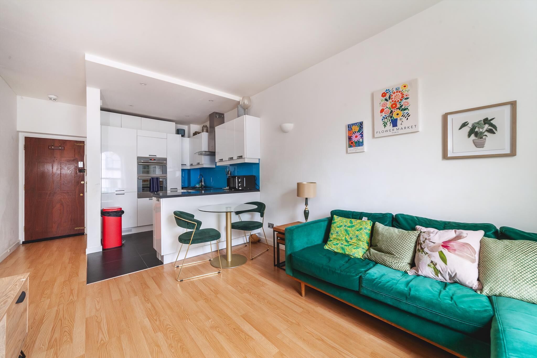 Una sala moderna con un sofá verde, una mesita redonda y una cocina al fondo.