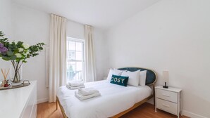 Ein ordentlich bezogenes Bett mit weißen Leinen und einem Kopfkissen mit dem Schriftzug "COSY".